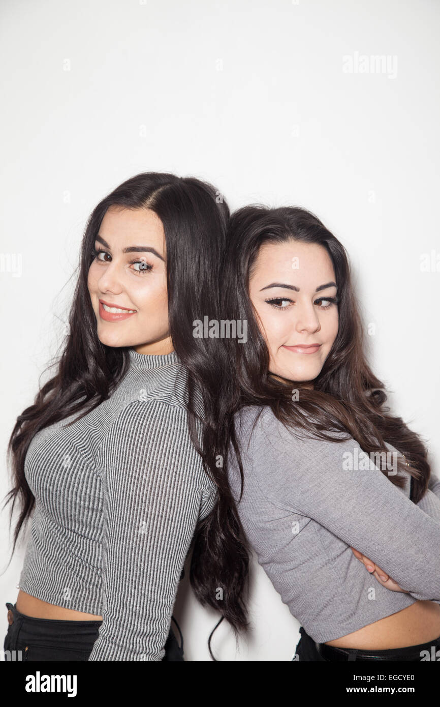 Two dark haired sisters leaning back to back. Stock Photo