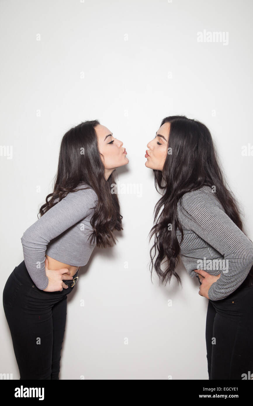 Two dark haired sisters leaning forward pretending to kiss each other. Stock Photo