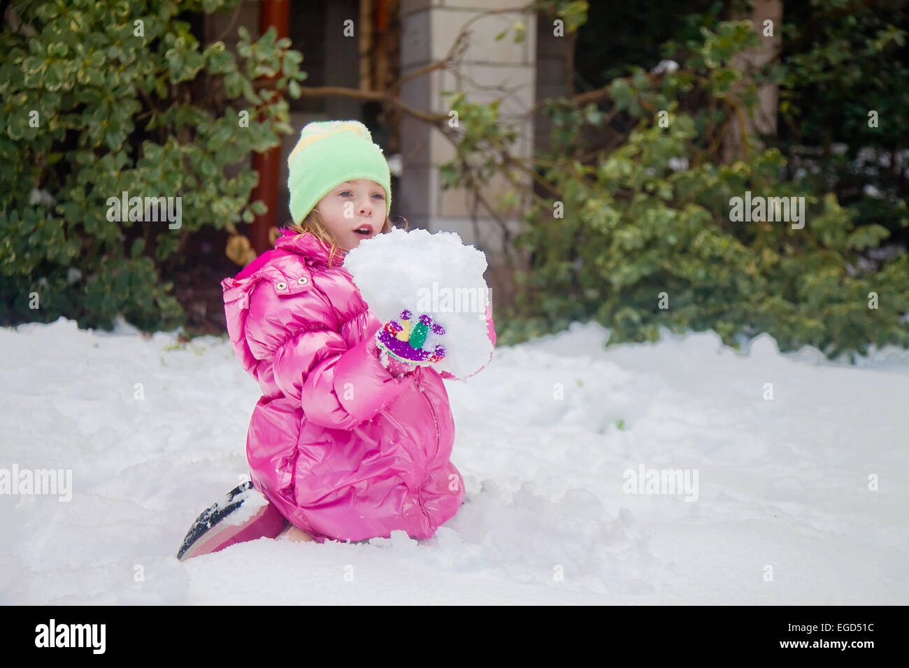 Cute blonde girl holding a huge snowball while sitting in the snow in her backyard in Jerusalem Stock Photo