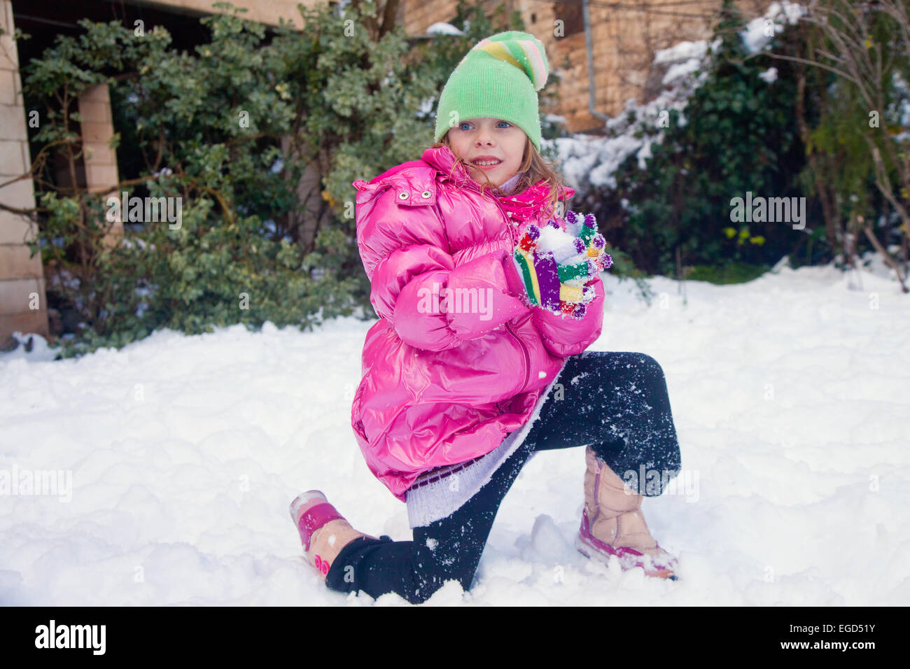 Little cute girl standing on one knee in the snow with a snowball in her hands Stock Photo