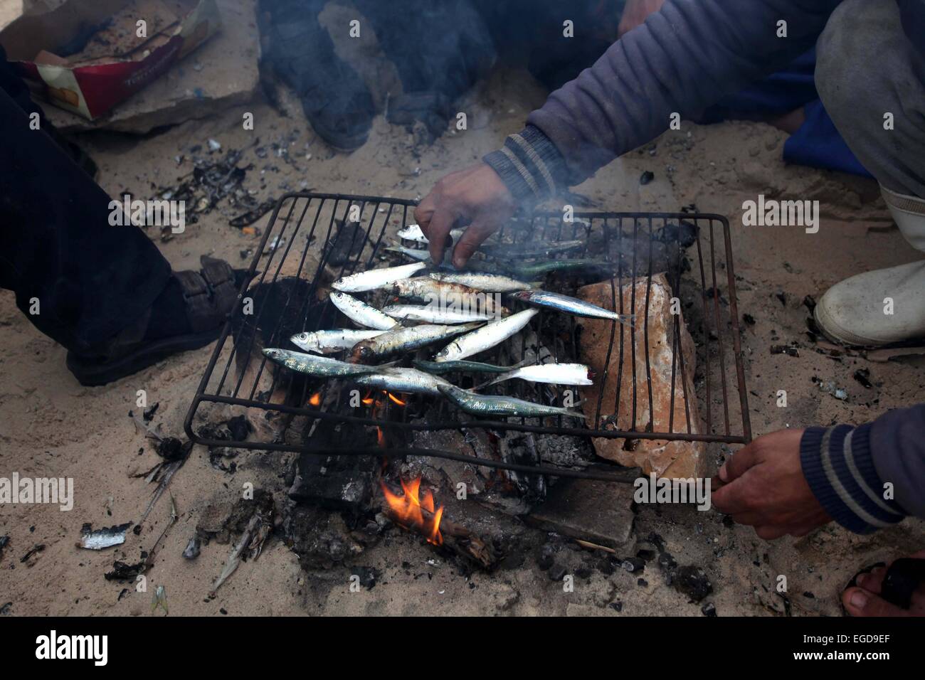 Gaza City, Gaza Strip, Palestinian Territory. 23rd Feb, 2015. Palestinian fishermen grill the fishes by the firewood at the port in Gaza City on February 23, 2015. Copious fish flowed to the coast of the Gaza Strip after fishermen break due to the storm that hit the region Credit:  Ashraf Amra/APA Images/ZUMA Wire/Alamy Live News Stock Photo