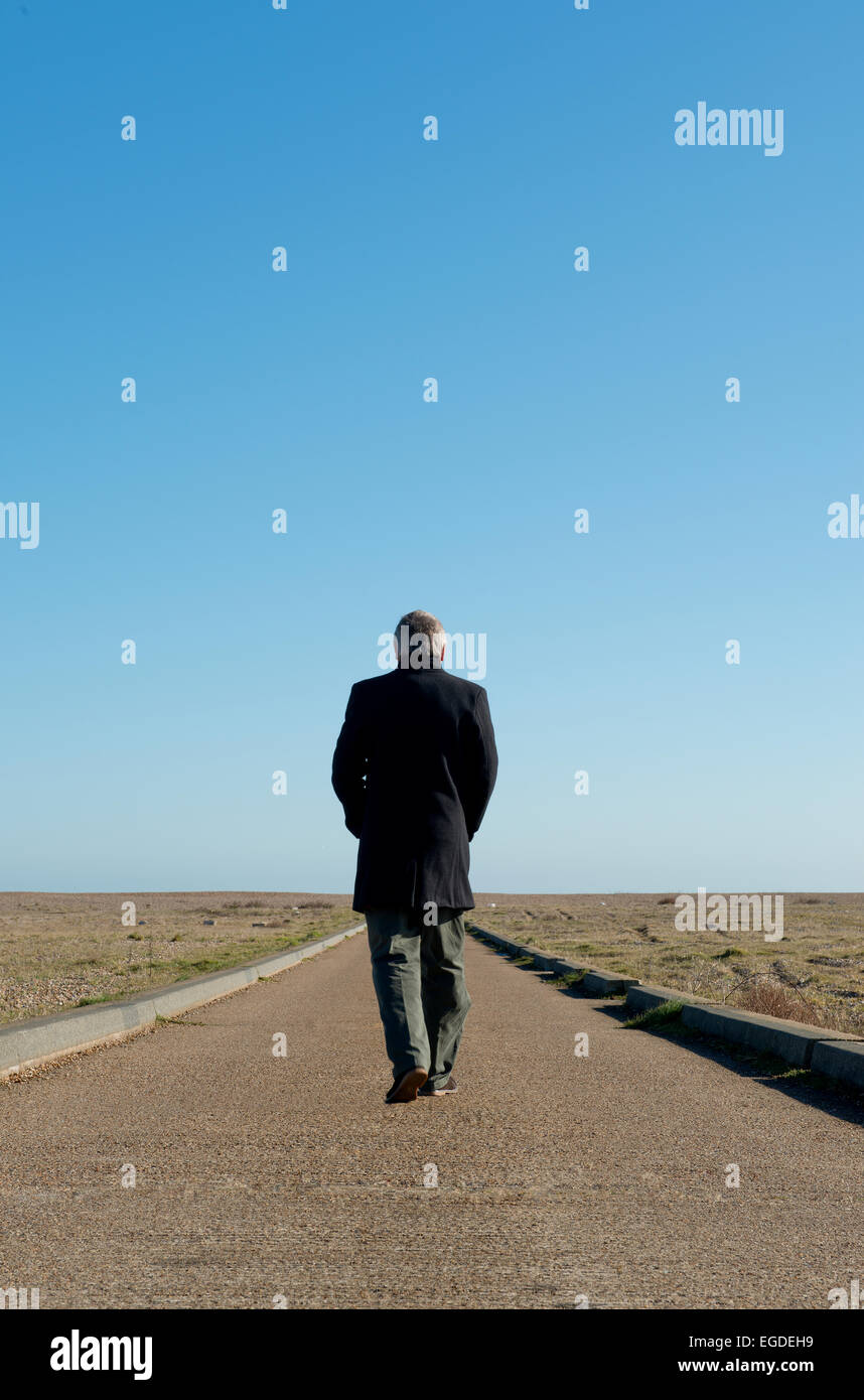 Man in a long coat, walking away from camera, along a never ending path into the horizon. Stock Photo
