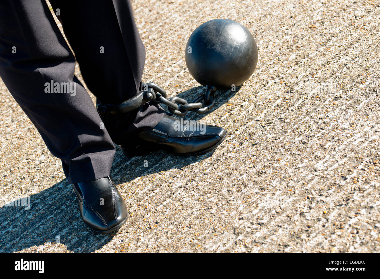 Angled,elevated view, of a businessman in a dark suit, attached to a ball & chain,. Stock Photo