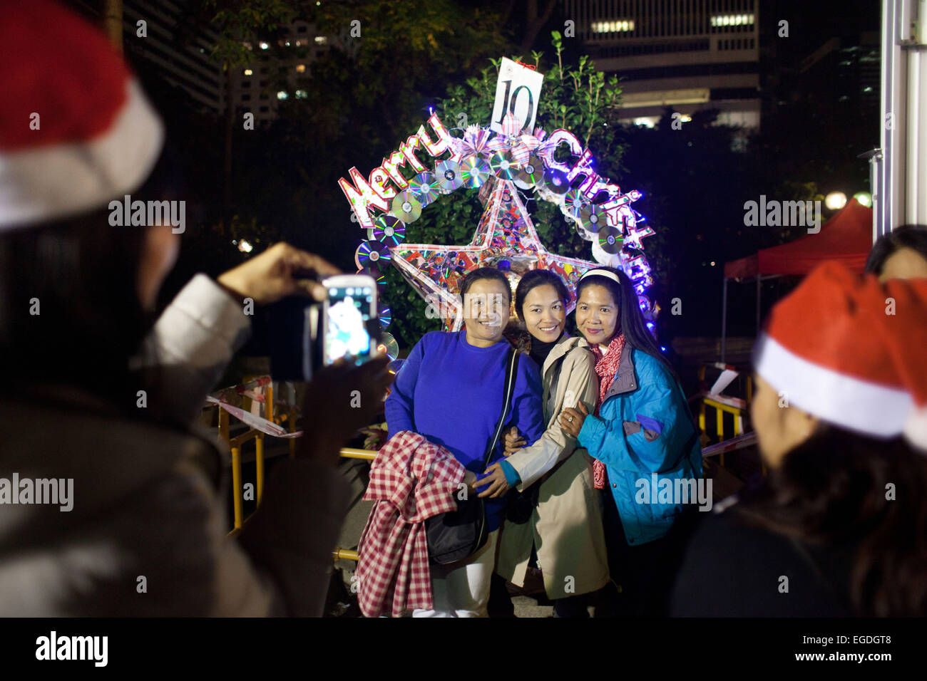 A group of Filipino women take photographs of each others with a Christmas decoration. It is Christmas Eve and thousands of Cath Stock Photo