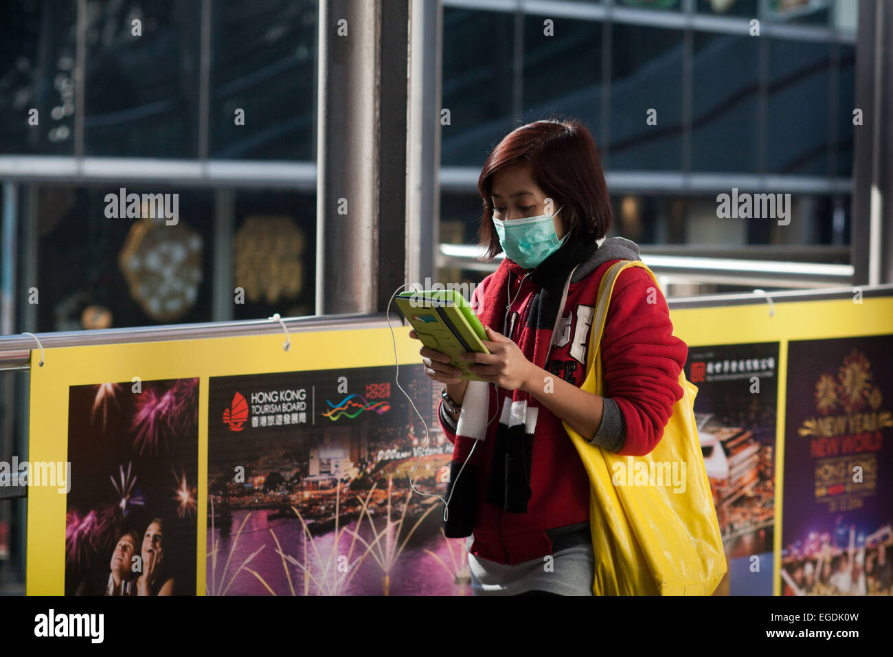 A woman with a yellow bag wears a green face mask. She walks and reads her iPad/tablet at the same time. Stock Photo