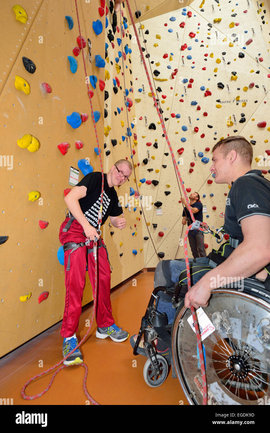 Wheelchair user belaying handicapped man at climbing, climbing gym