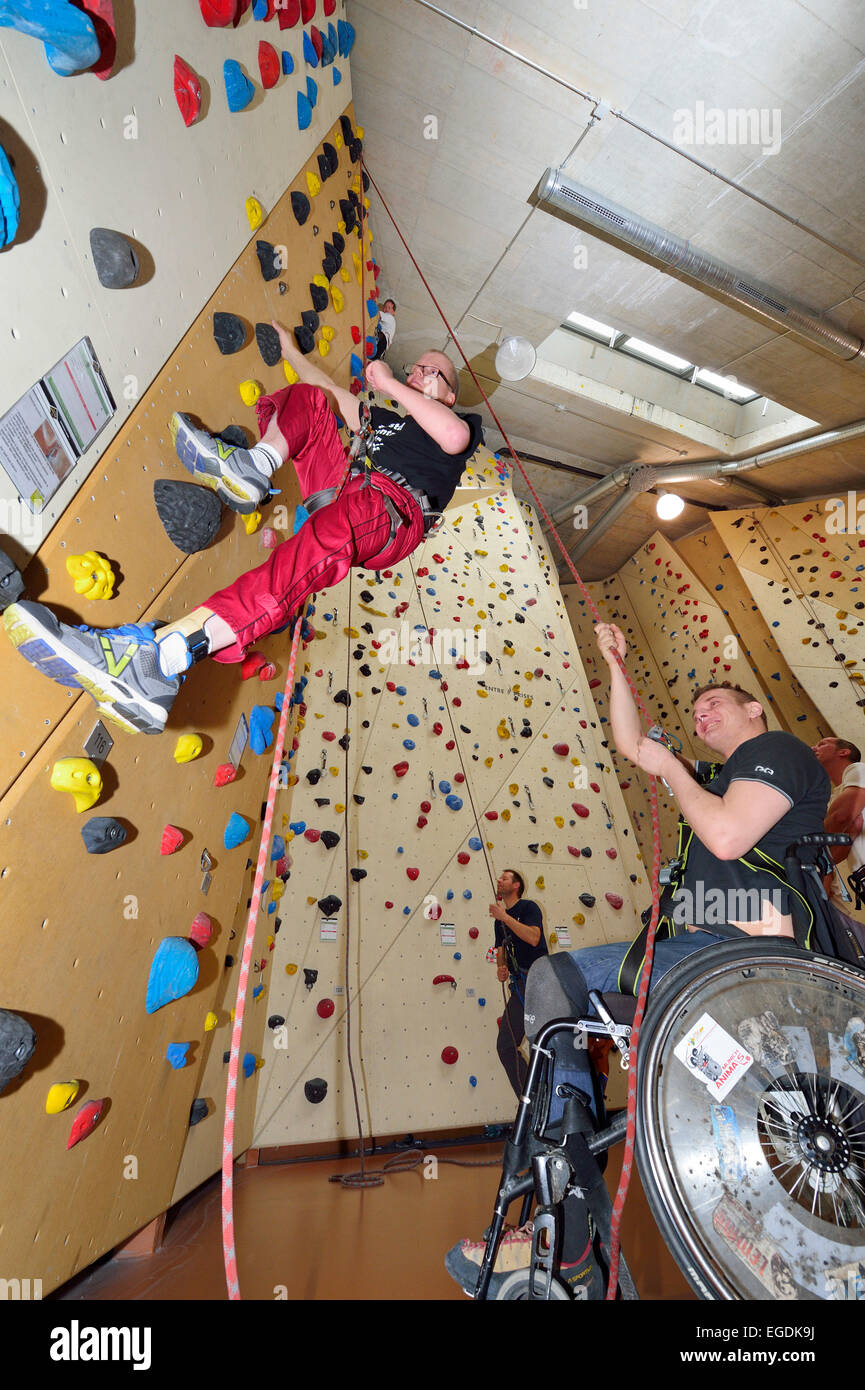Wheelchair user belaying handicapped man at climbing, climbing gym