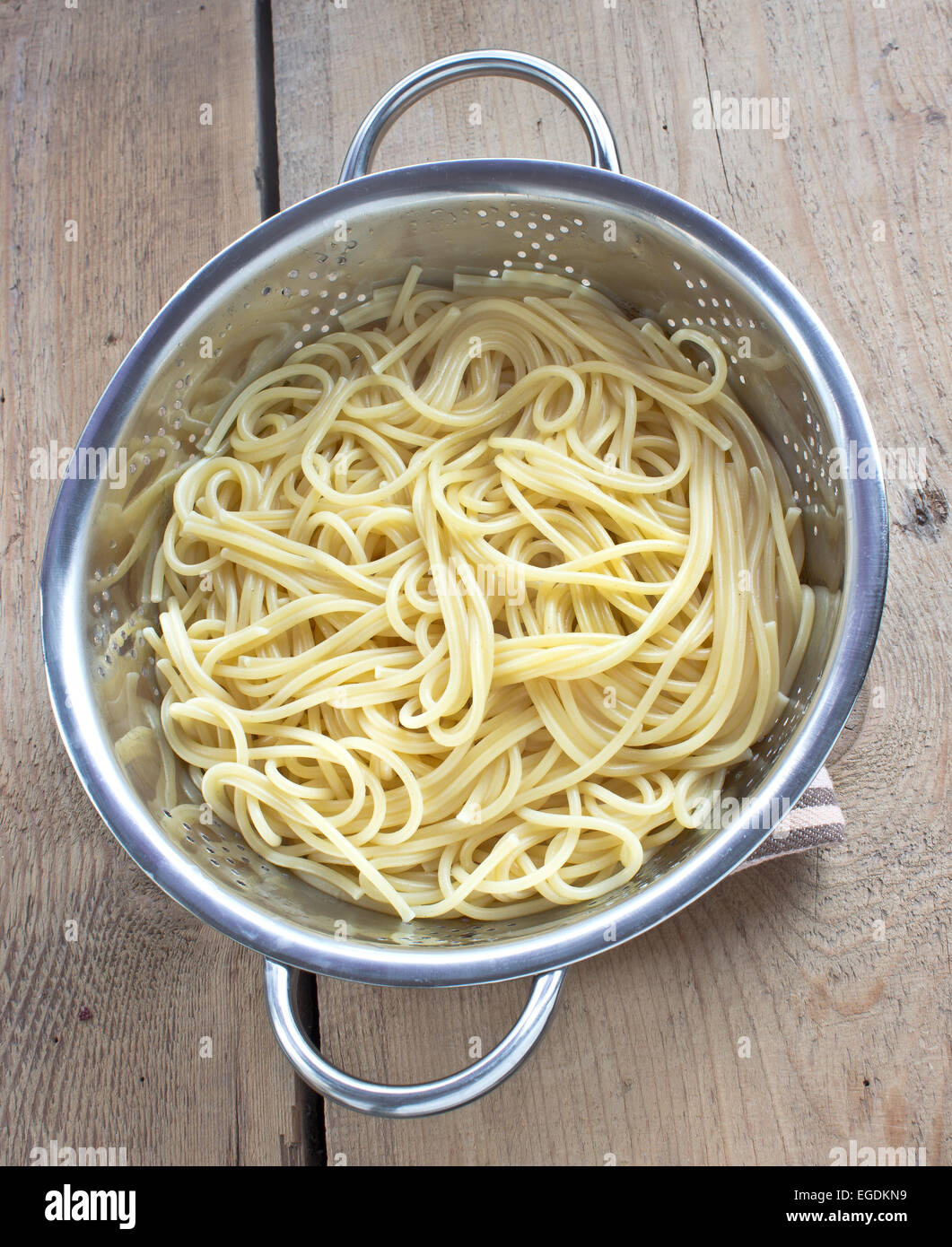 Fresh cooked spaghetti in strainer on wooden table Stock Photo