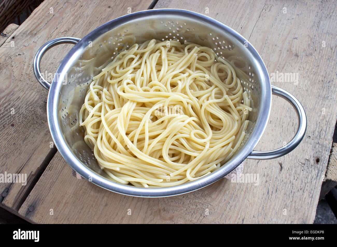 Fresh cooked spaghetti in strainer on wooden table Stock Photo