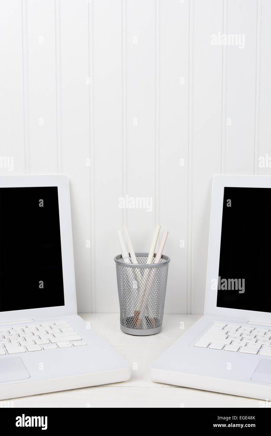 Closeup of two laptops in a white work station with a pencil cup in the middle. The computers are at an angle with blank screens Stock Photo