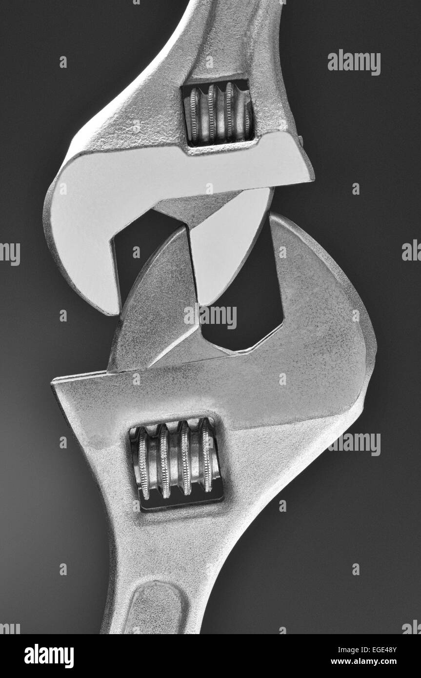 Closeup of two adjustable wrenches locked together over a light to dark gray background. Stock Photo
