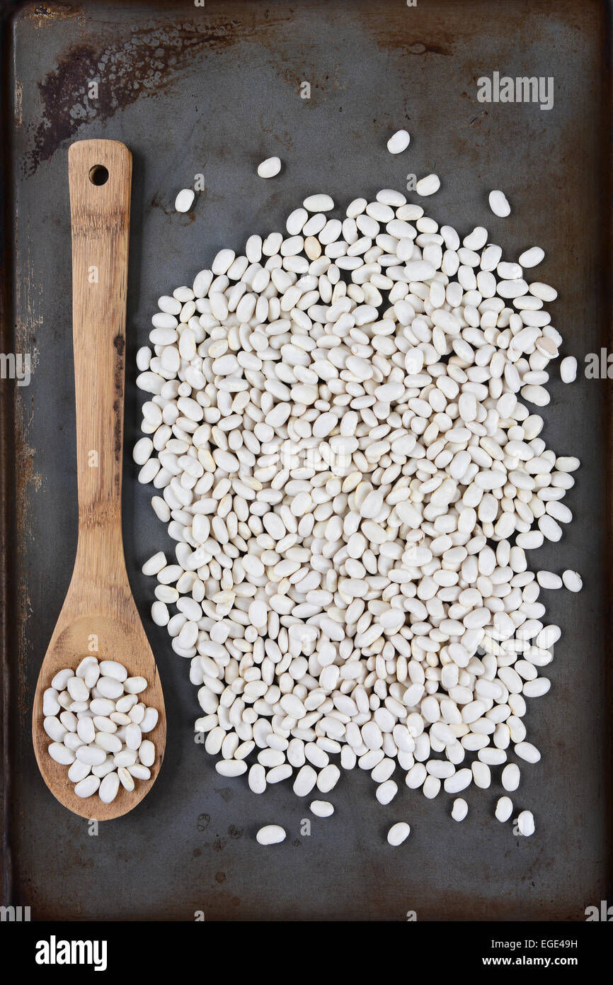 High angle shot of white beans and a wooden spoon on a used metal baking sheet. Vertical Format. Stock Photo