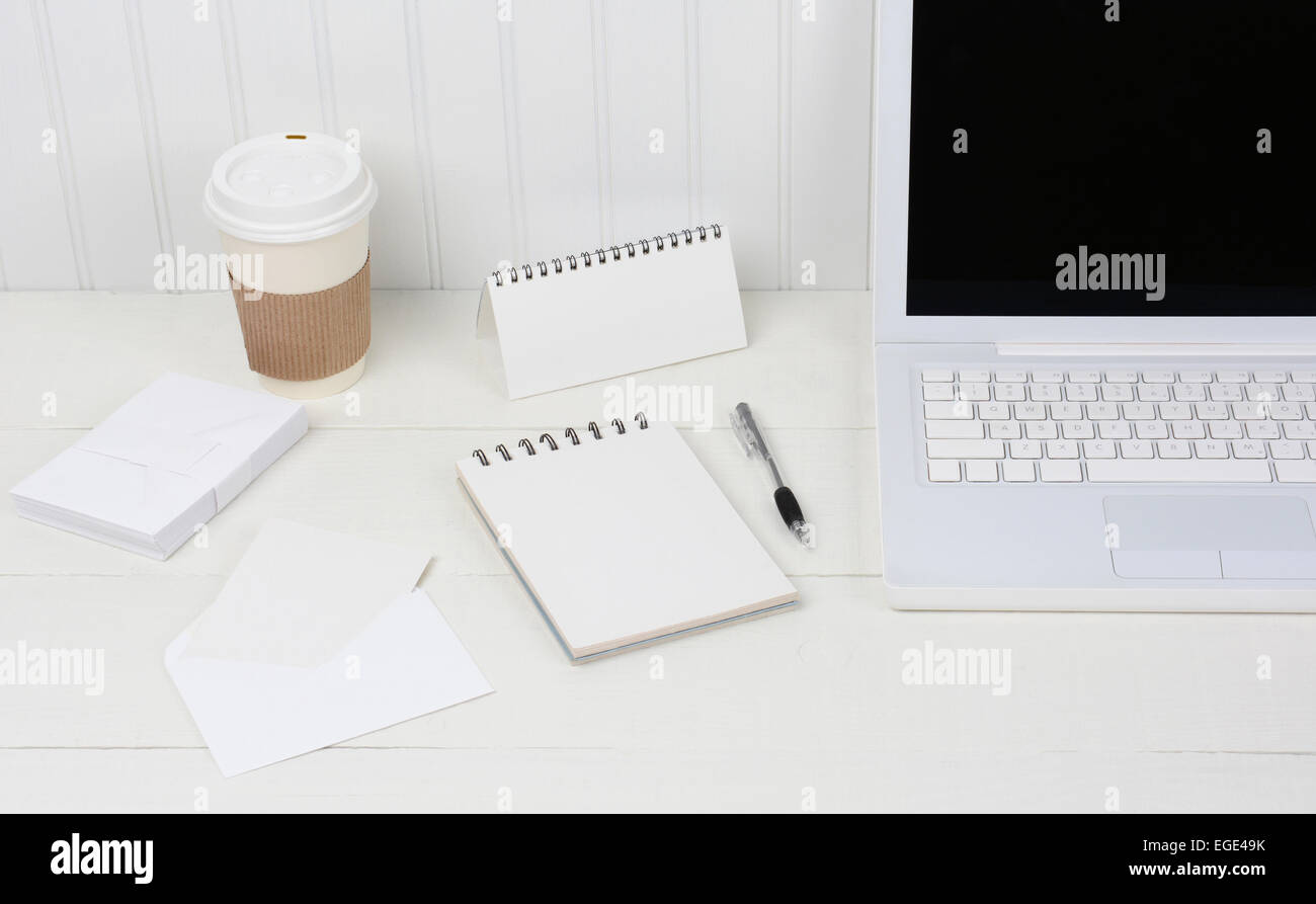 Closeup of a neat white desk with Laptop, disposable coffee cup, note pad, envelopes and pen. A wood desk with a beadboard wall Stock Photo