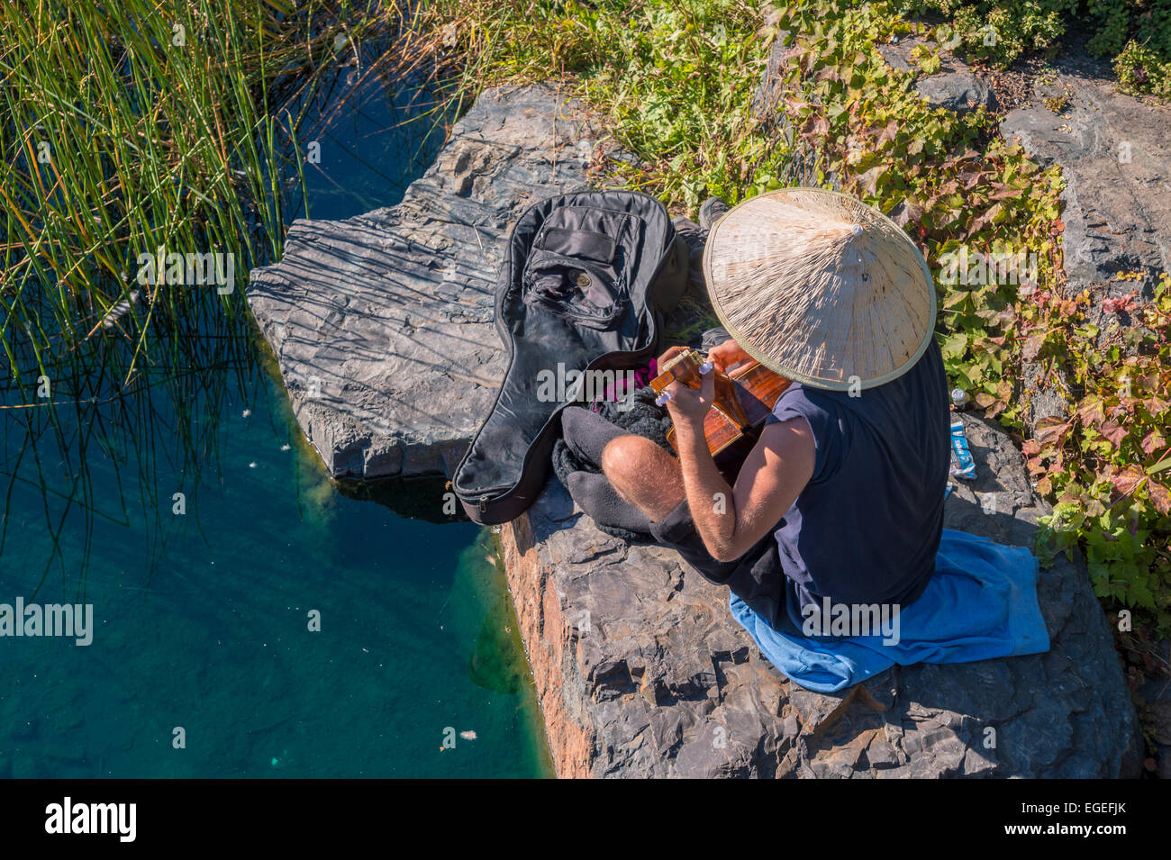 Man with Bamboo hat playing guitar on a rock at Lafontaine Park in Montreal, during the Indian Summer Stock Photo