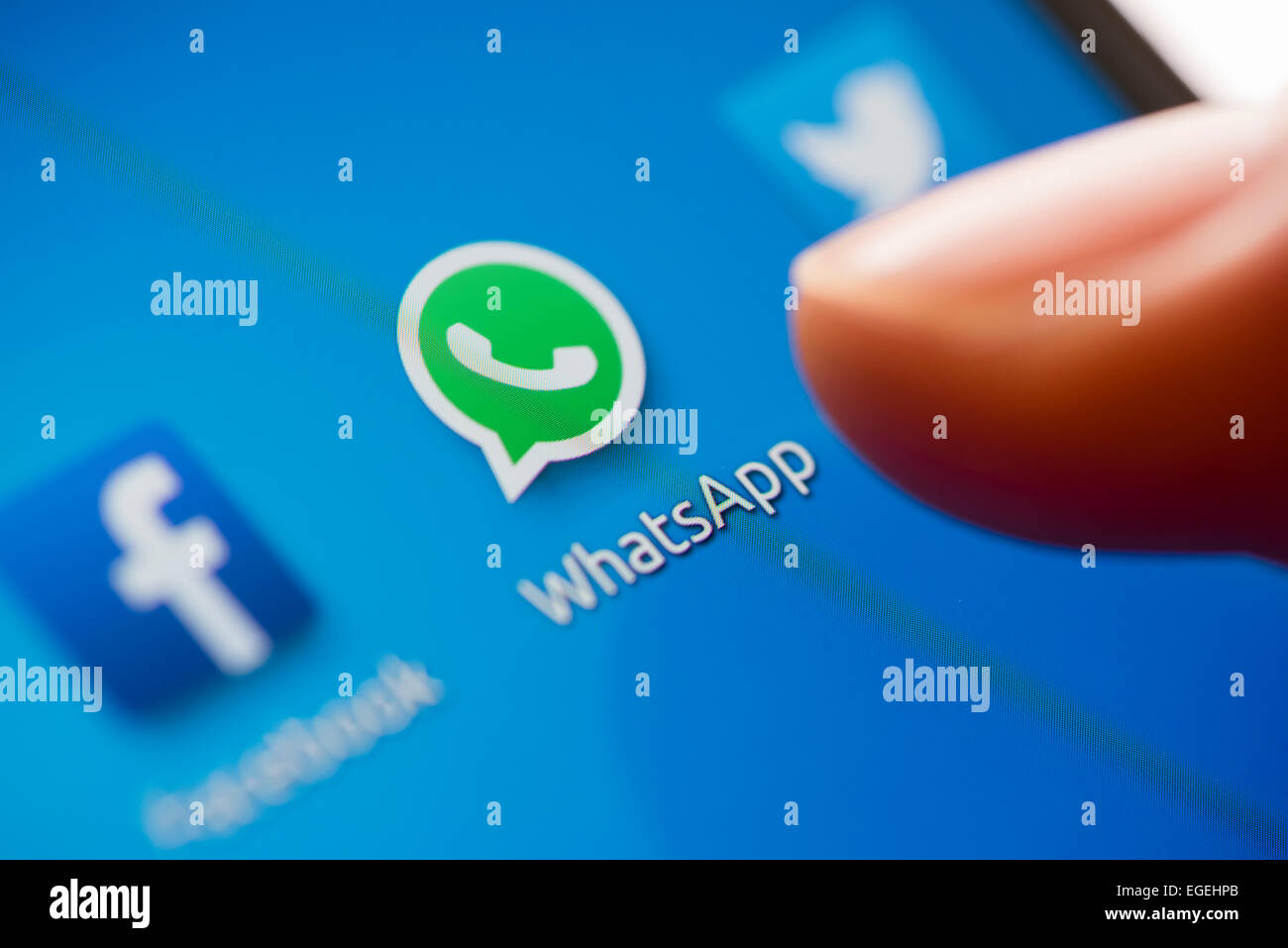A smartphone user's finger above the icon of 'WhatsApp', facebook and twitter apps on a mobile phone's touchscreen. Stock Photo