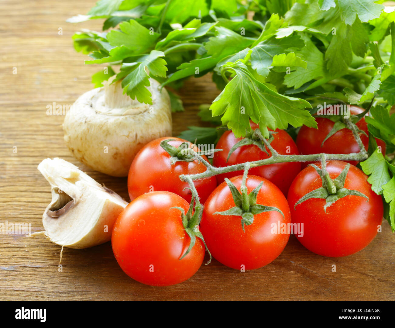 Mix vegetables (tomatoes, cucumbers, mushrooms, herbs) on a wooden table Stock Photo