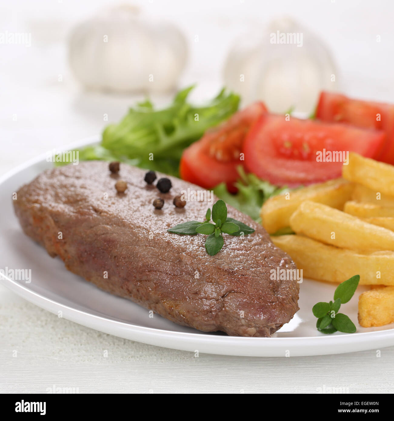 Fried beef steak meat meal with fries, vegetables, tomatoes and lettuce on plate Stock Photo