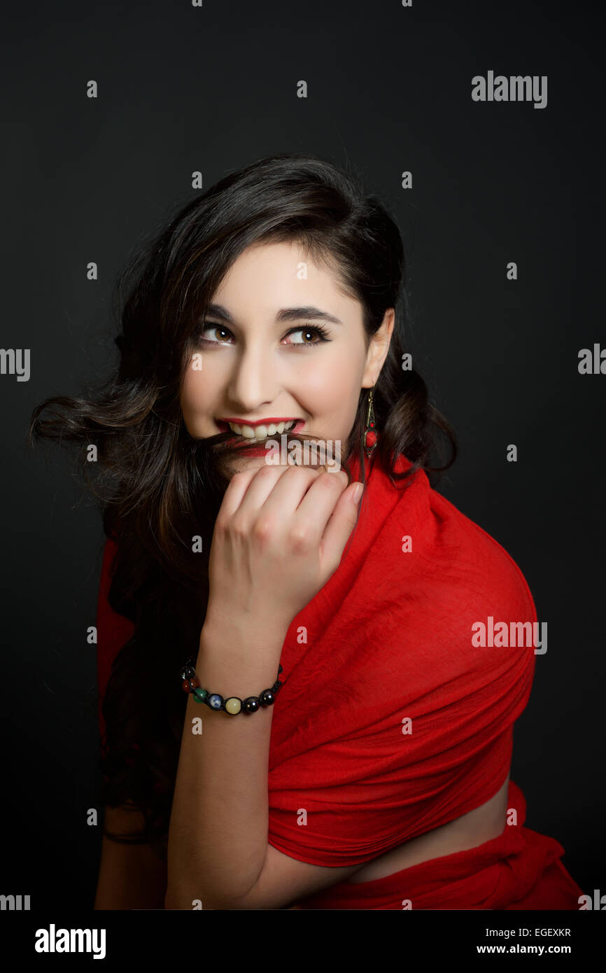 Beautiful biting hair hispanic girl in red on black background Stock Photo