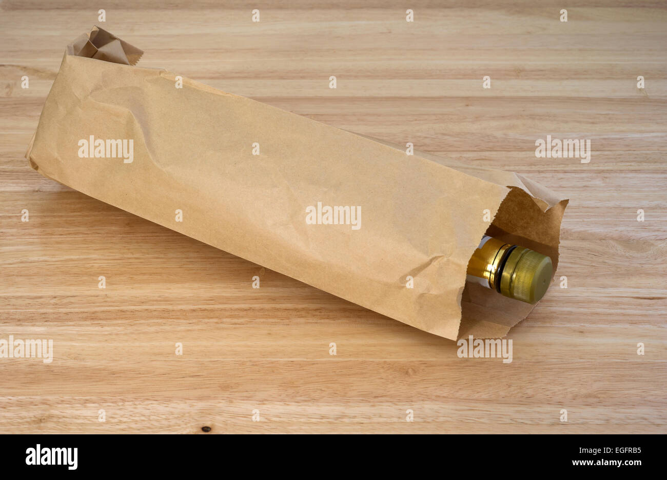 An unopened bottle of whiskey in a plain brown paper bag laying on a wood table top. Stock Photo