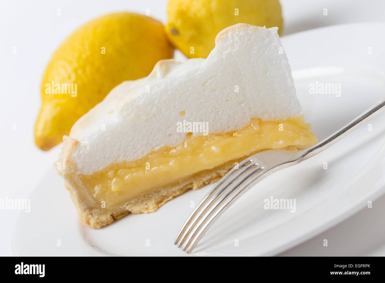 Homemade lemon meringue pie, a classic of European dessert cuisine, with lemons and a fork, shot at an angle Stock Photo