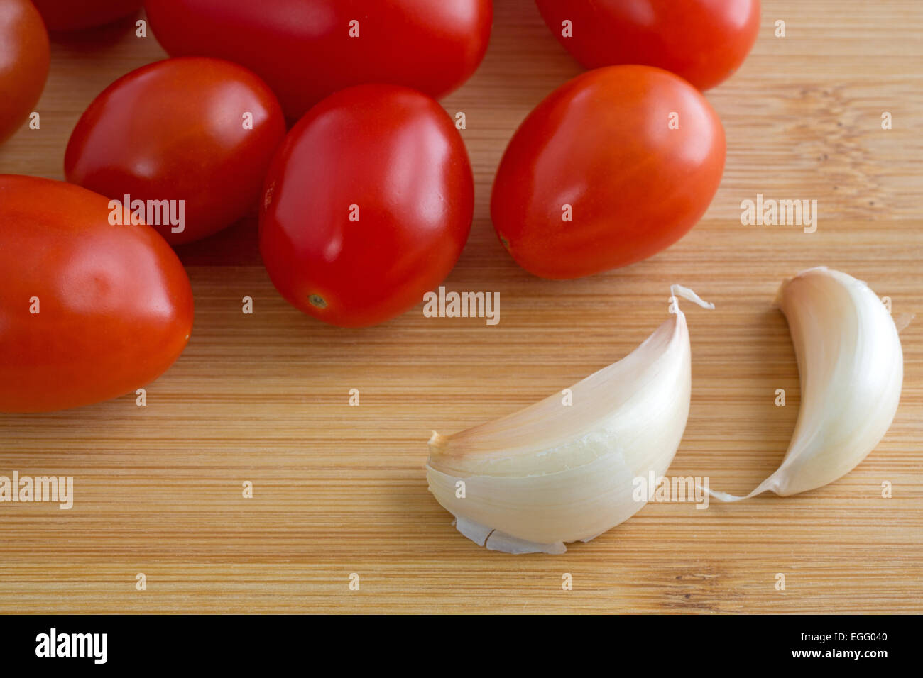 Close view of two garlic cloves with grape tomatoes on a wood cutting board. Stock Photo