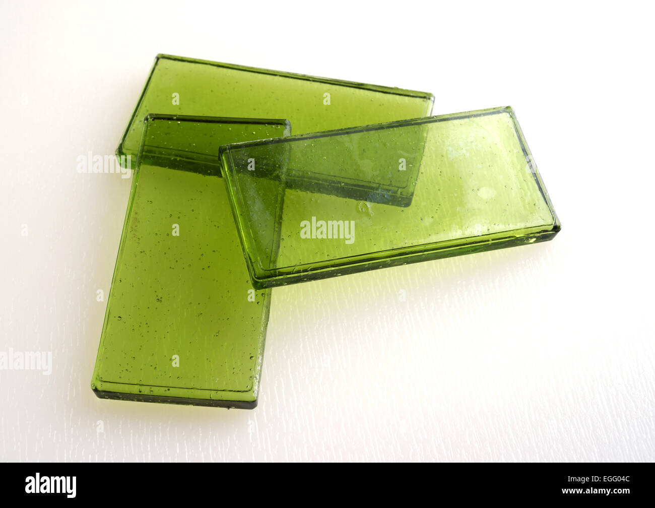 Three green tinted glass tiles arranged on a white background illuminated by natural light. Stock Photo