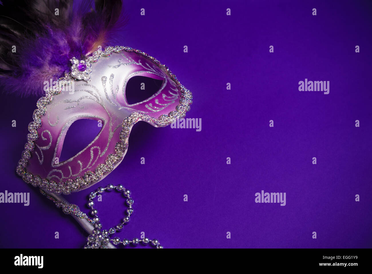 A purple mardi gras mask on a purple background with beads. Carnival