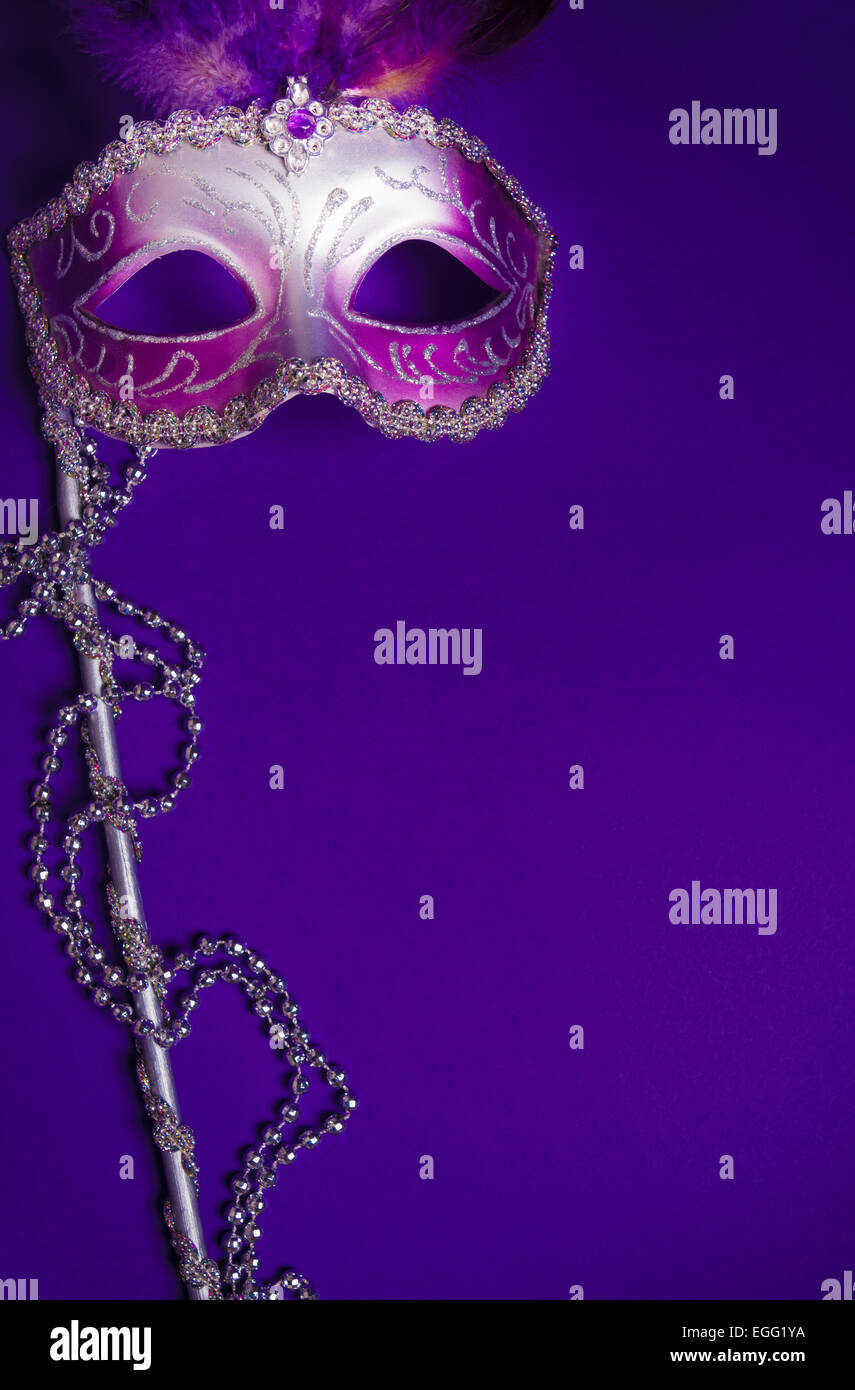 A purple mardi gras mask on a purple background with beads. Carnival