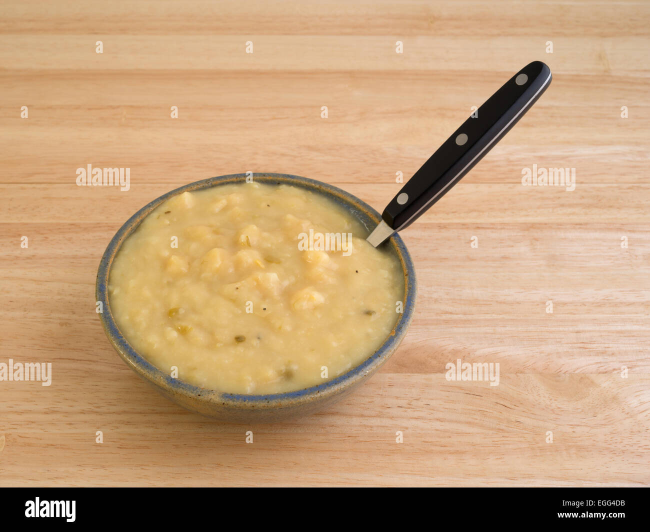 A serving of potato and leek soup in a bowl with a black handle spoon on a wood table top. Stock Photo