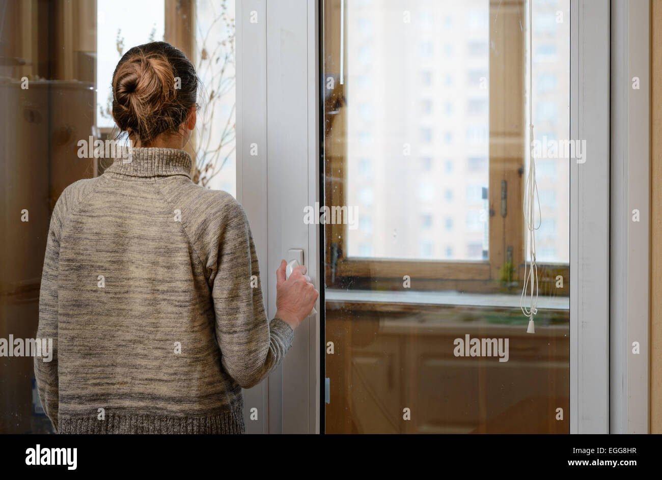 A woman is looking the city through the window during a sad winter day Stock Photo
