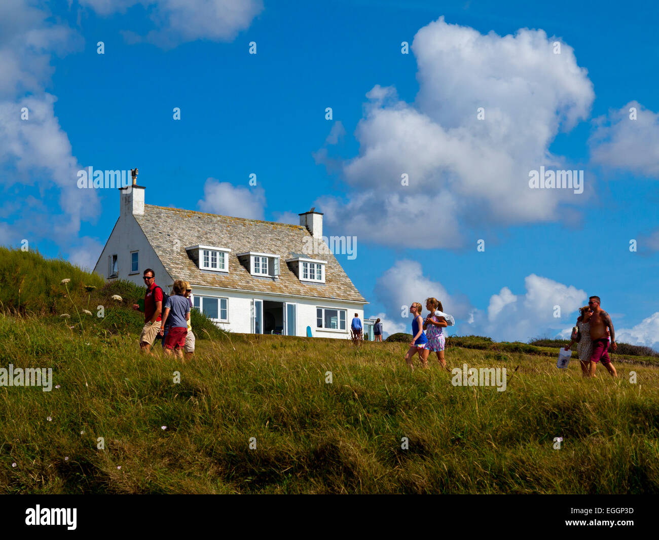 People walking past a white house on the South West Coastal Path at Daymer Bay in North Cornwall England UK Stock Photo