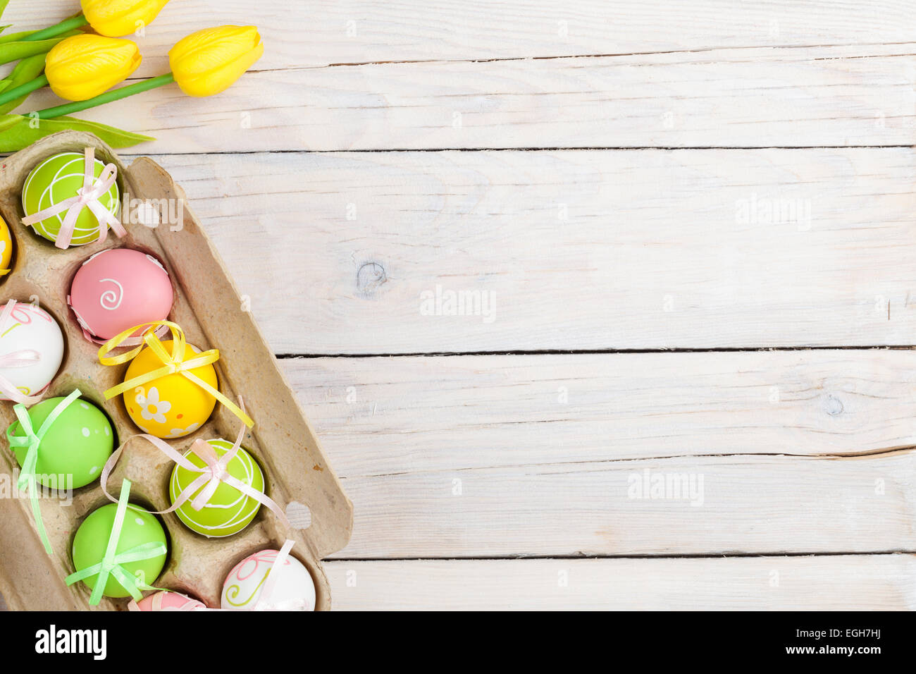 Easter background with colorful eggs and yellow tulips over white wood ...
