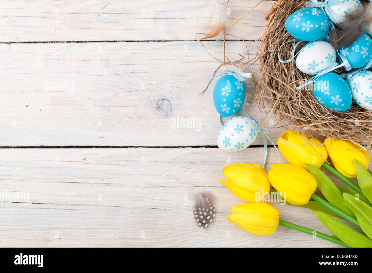 Easter background with colorful eggs and yellow tulips over white wood ...