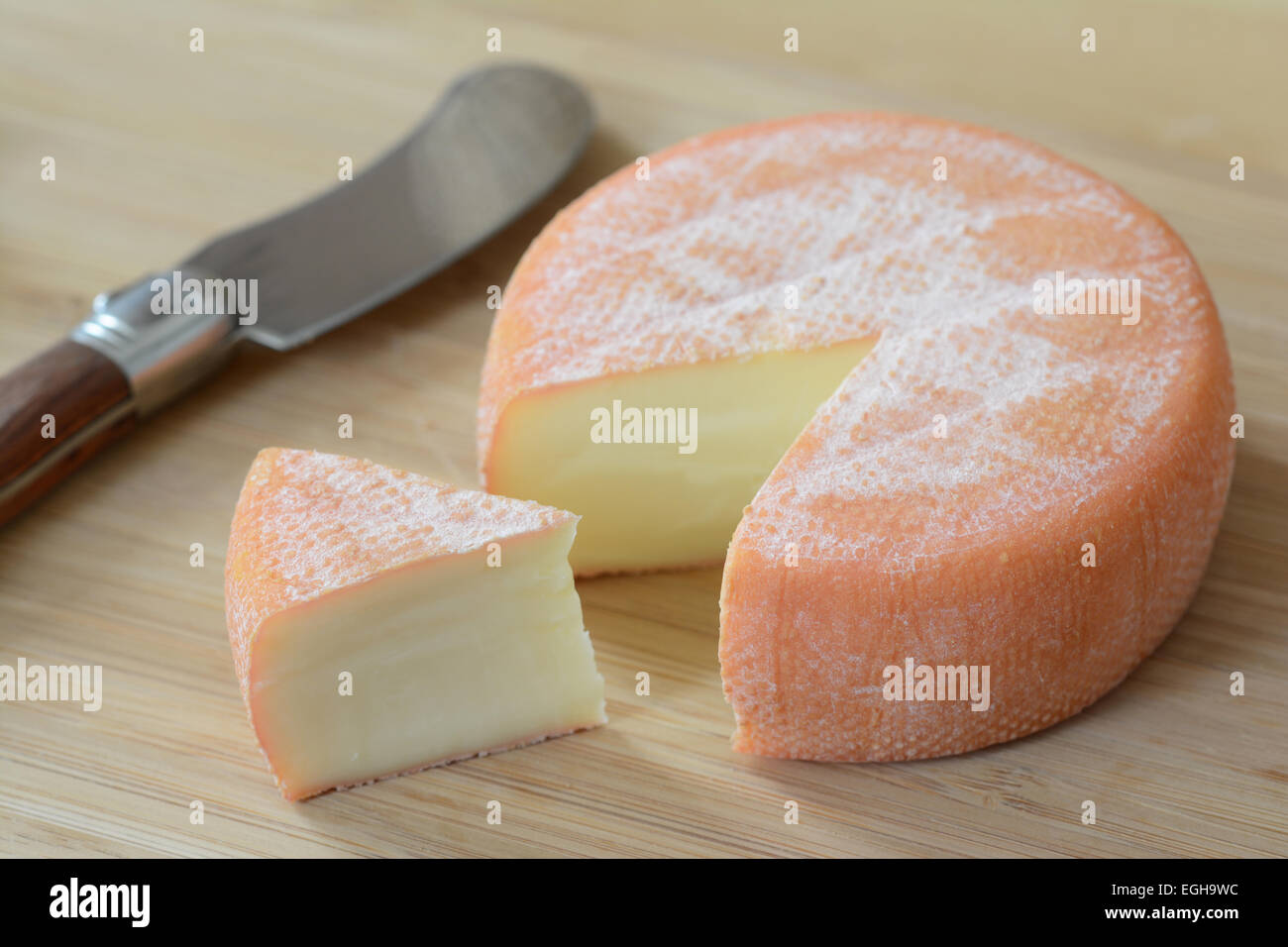 A full wheel brie cheese with one slice cut and a knife Stock Photo