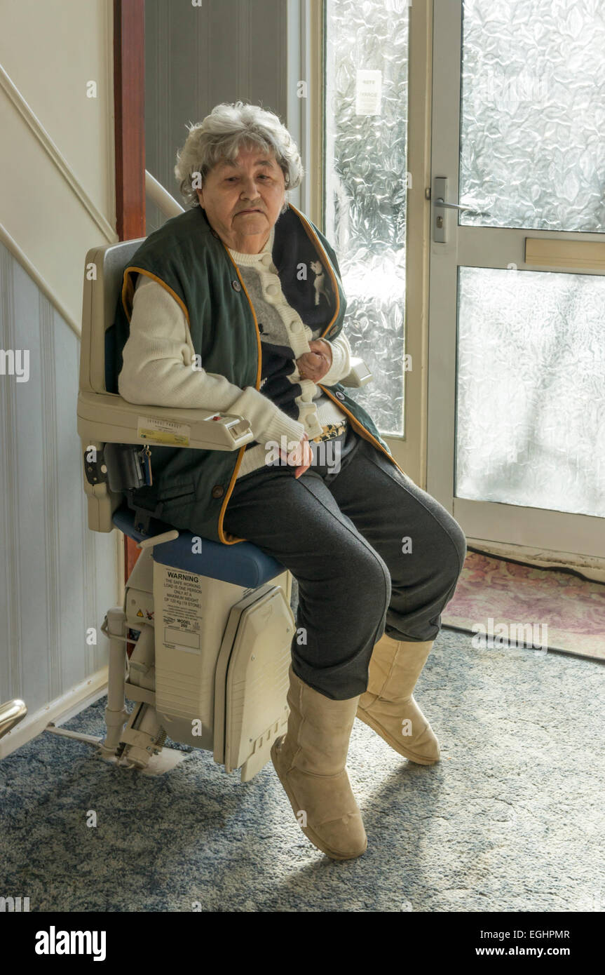 An elderly lady using a stair lift to go upstairs in her own home. Stock Photo
