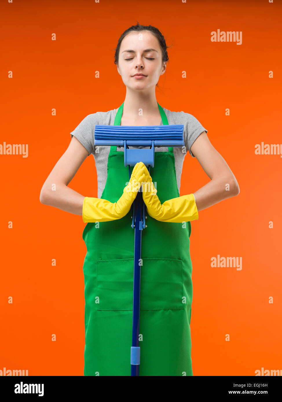 happy cleaning lady meditating while holding mop, on orange background