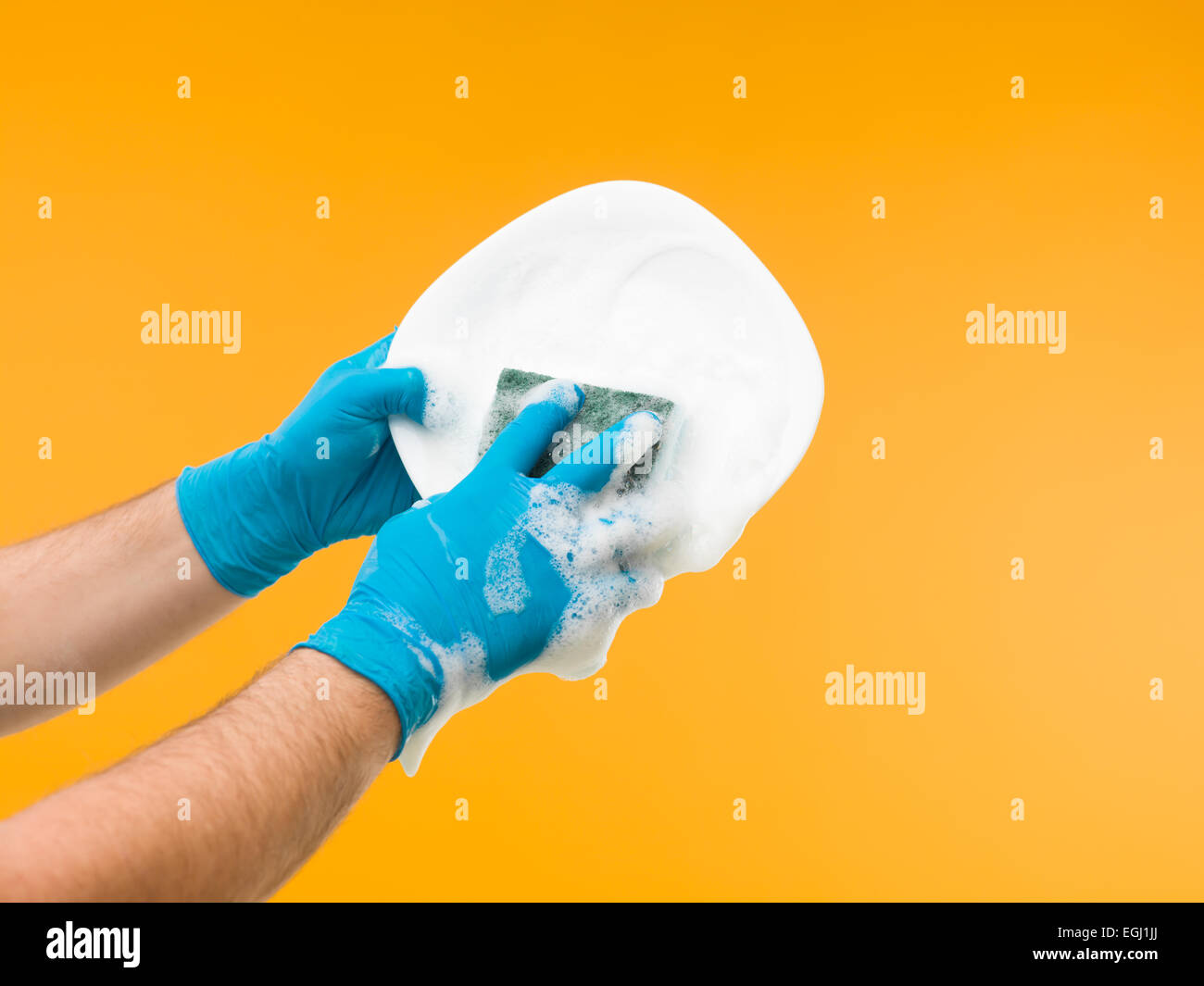hands wearing rubber gloves washing dish with detergent against yellow