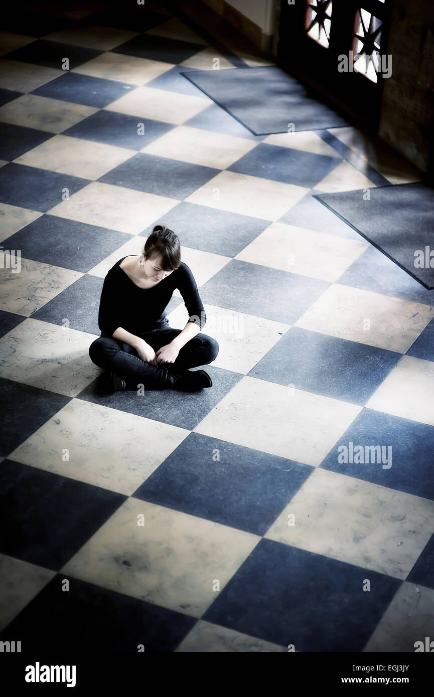 Young woman, cross-legged on tiled floor, Stock Photo