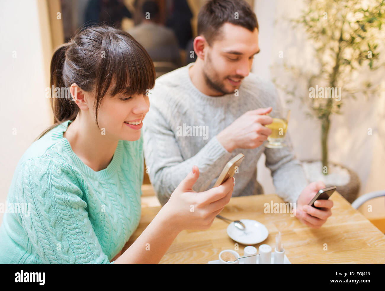 smiling couple with smartphones drinking tea Stock Photo - Alamy
