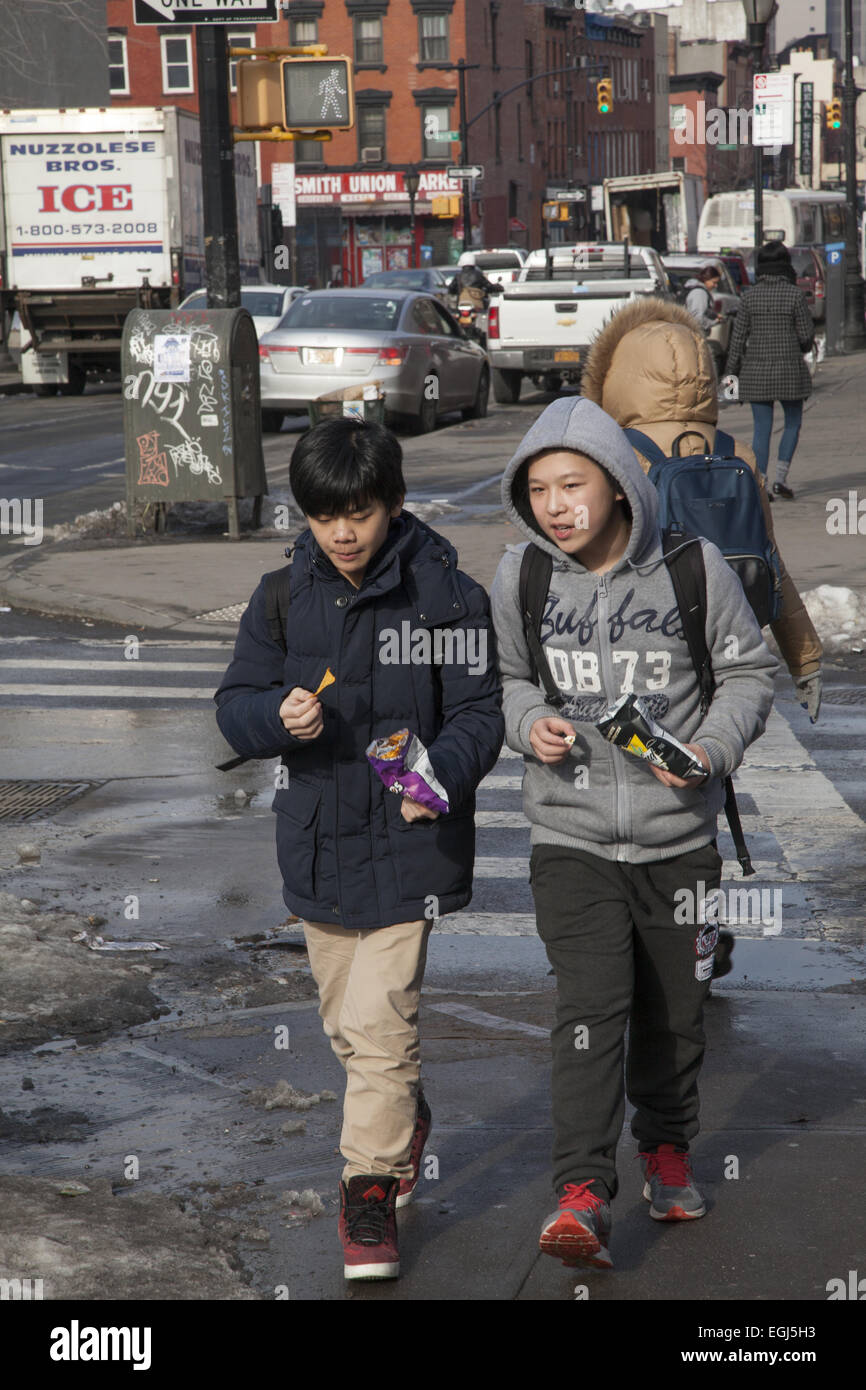 Pre-teen boys snack as they walk home after school along Smith Street in the Carroll Gardens neighborhood of Brooklyn, NY. Stock Photo