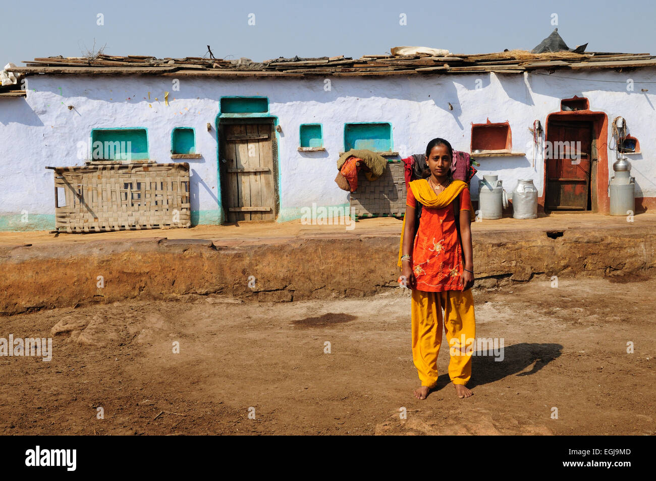 Indian girl wearing brignt orange and yellow clothes standing outside her house kalpi Village Rajasthan India Stock Photo