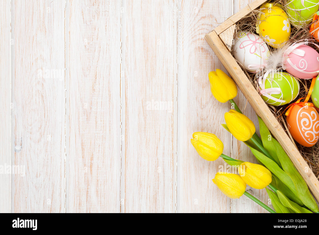 Easter background with colorful eggs and yellow tulips over white wood ...