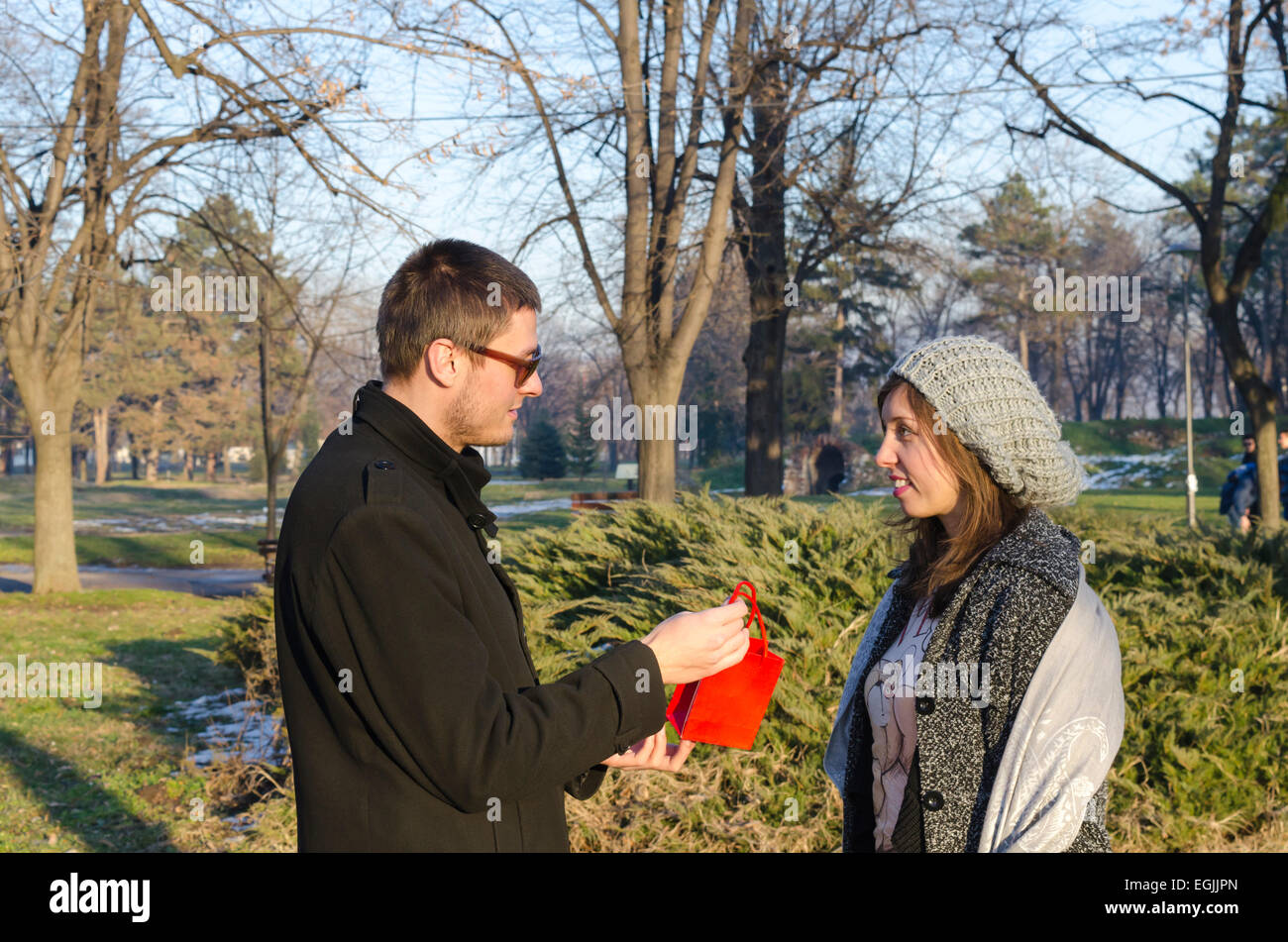 Tall boy giving a present to a girl outdoors in a park Stock Photo