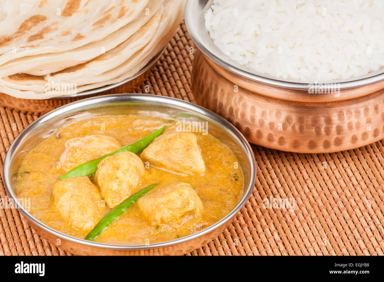 Indian chicken curry meal with rice & parotta (Indian bread) served in authentic copper utensils. Green chilli used as garnish. Stock Photo