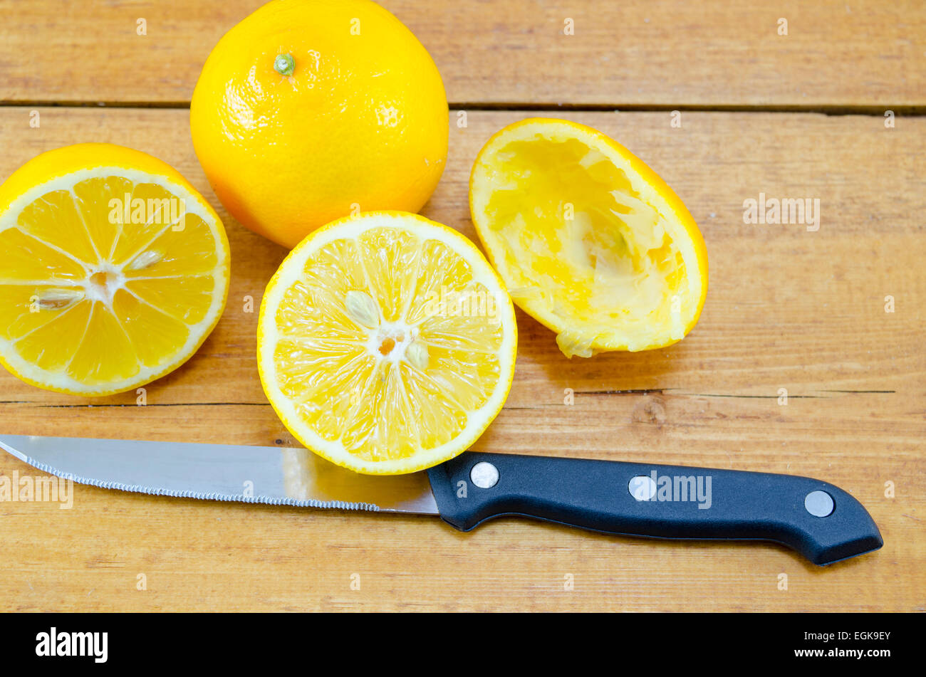 Halved lemon and a squeezed half together with a knife on a wooden table Stock Photo
