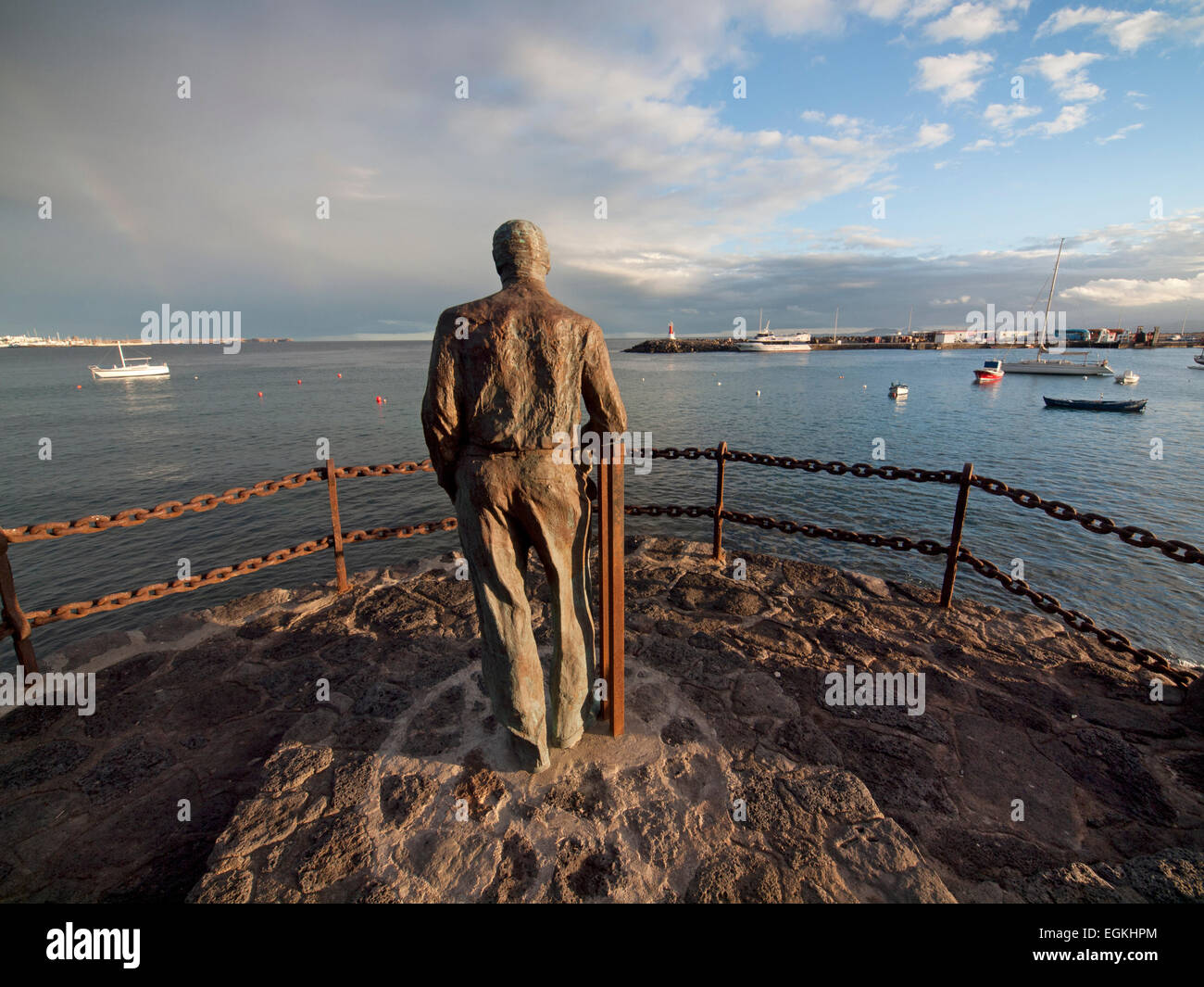 A statue of a man looking out to sea, on the harbor wall in Playa