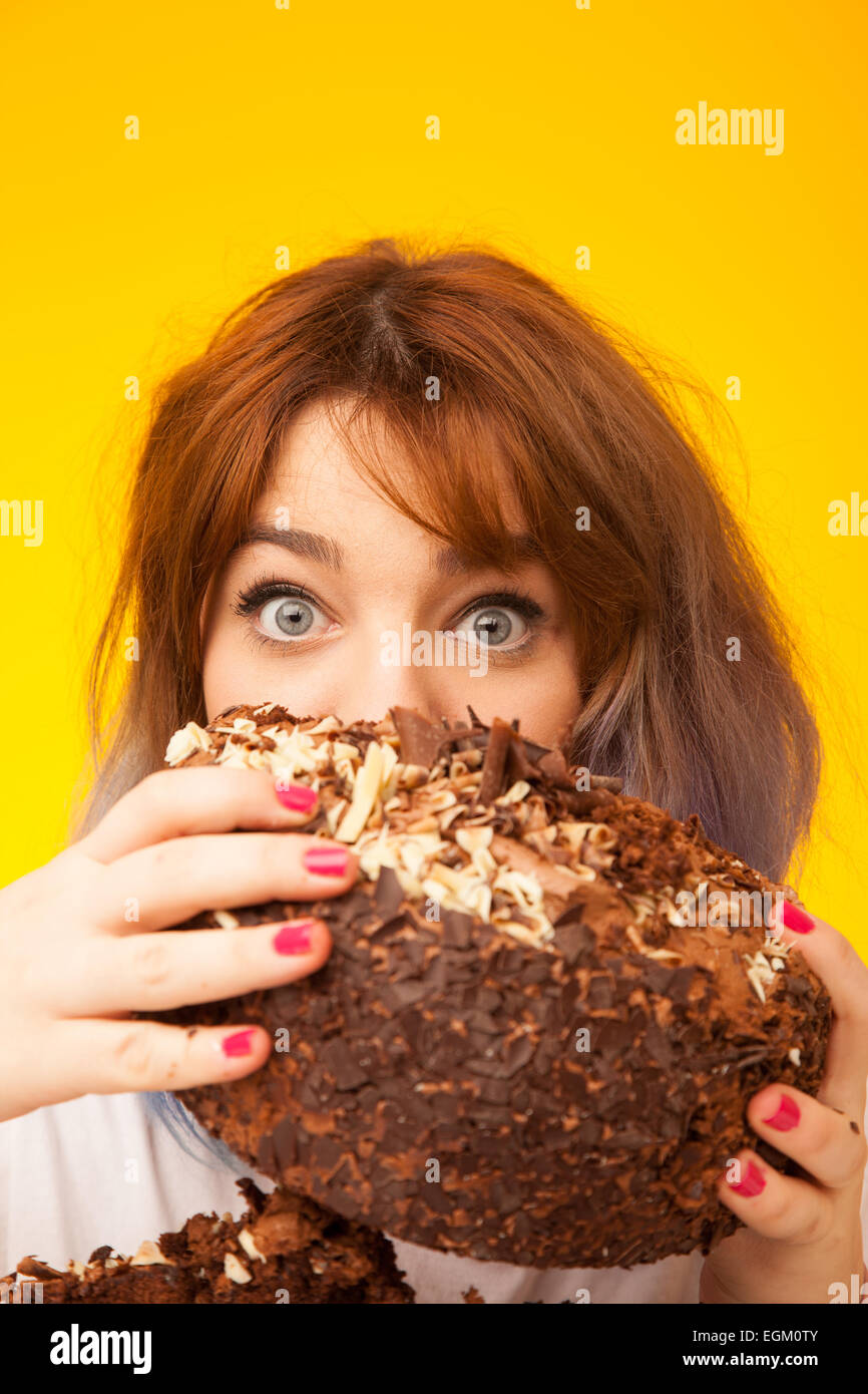 Young woman holding a large chocolate cake in front of her face. Stock Photo