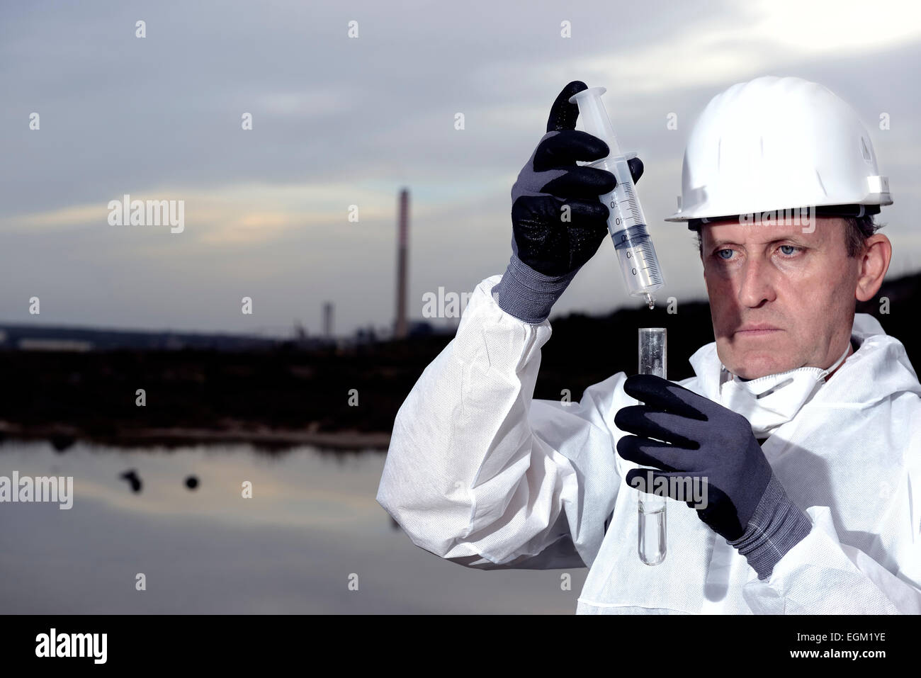 Worker in a protective suit examining pollution in the water at the industry. Stock Photo