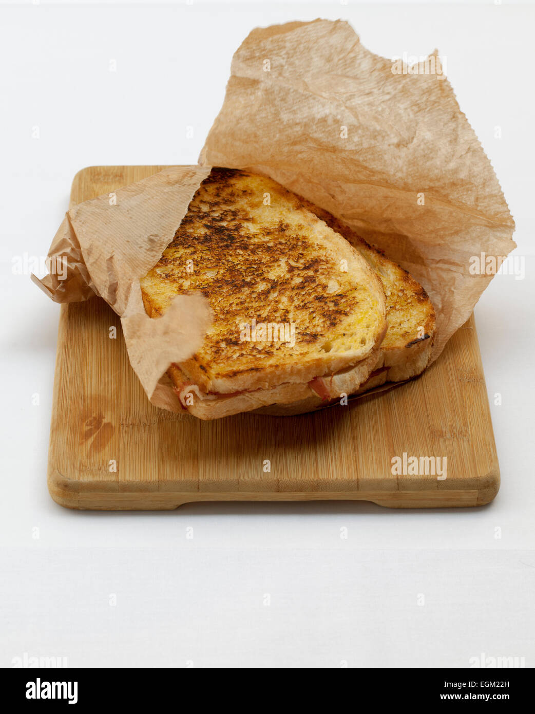Toasted Gourmet Ham and Cheese Sandwich in Brown Paper Bag on wooden bread board Stock Photo