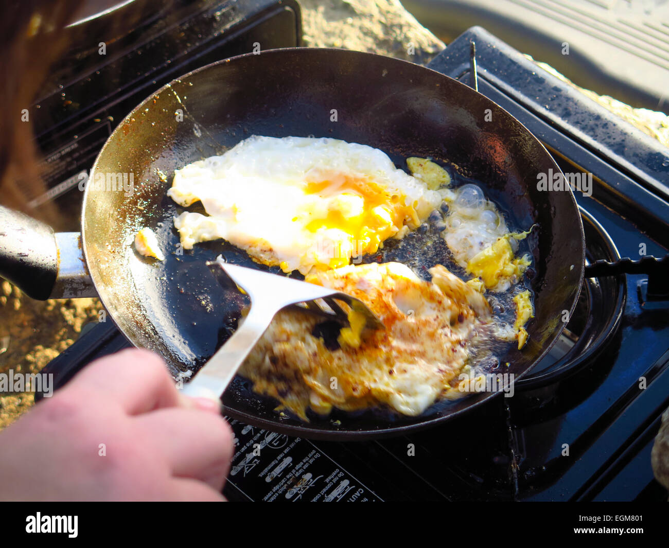 Frying eggs in pan on camping gas stove Stock Photo